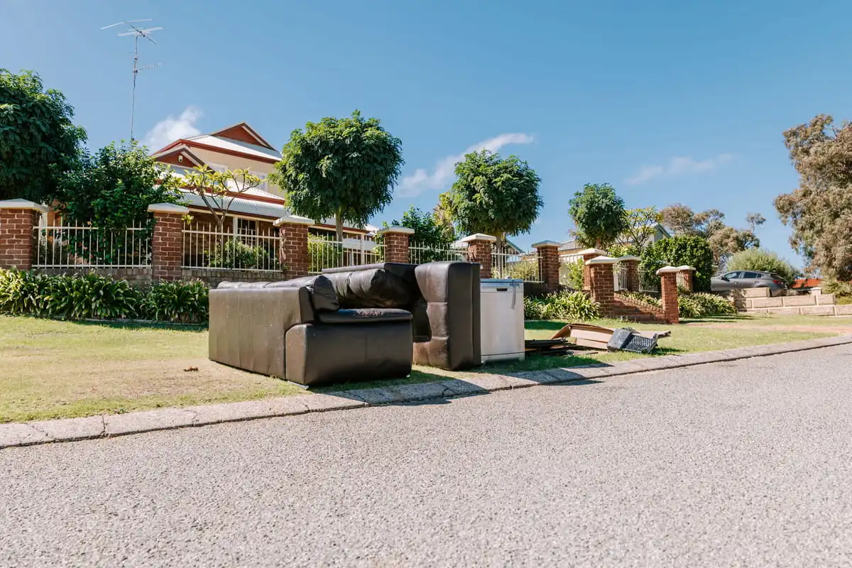 Old furniture and household junk, including a couch and appliances, left on a suburban verge